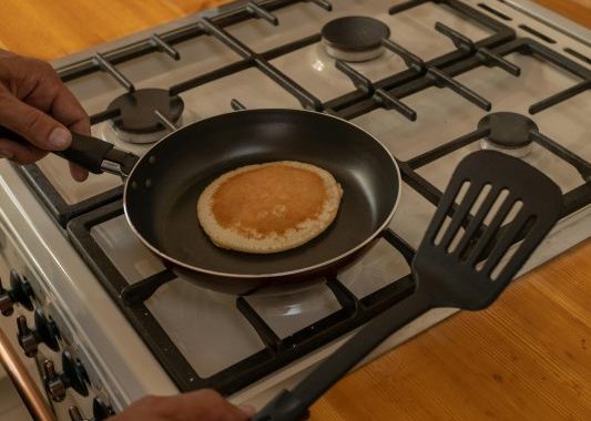 A hand holding a pan with pancake on it and another hand holding a spatula